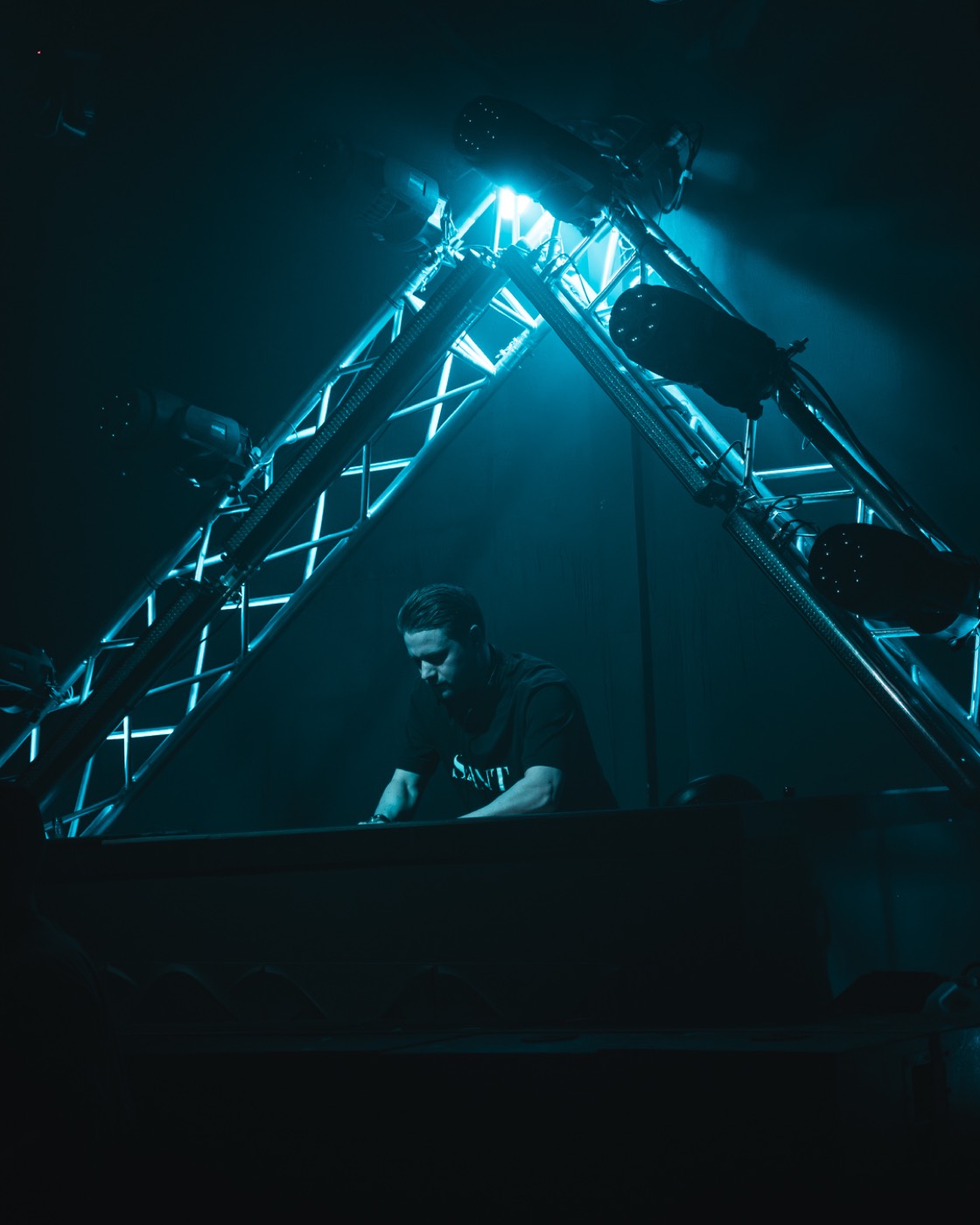 DJ am Pult unter dem türkis beleuchteten Traversendreieck
