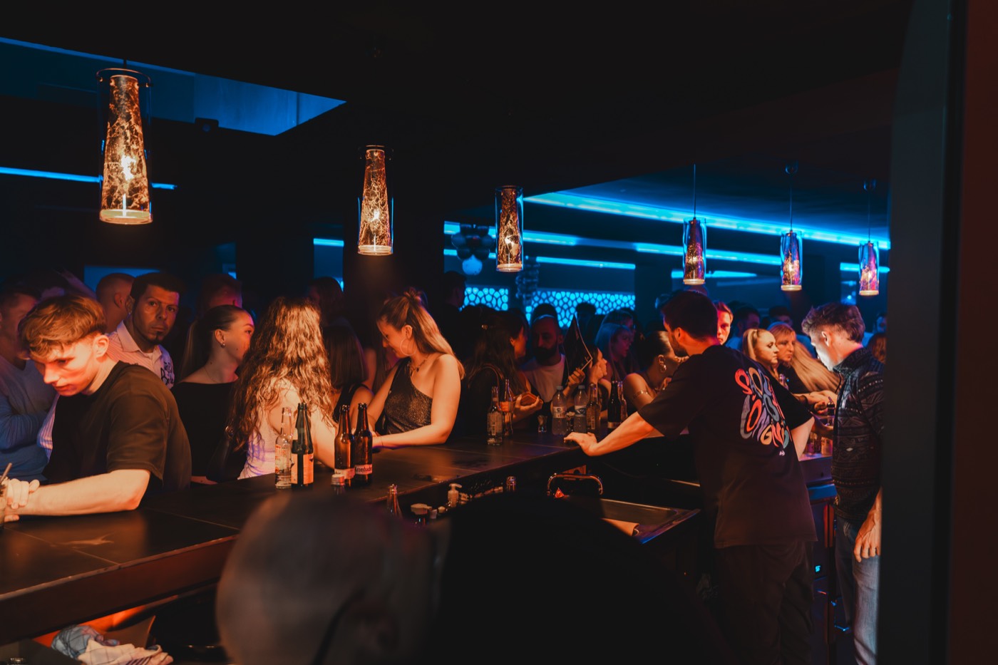 Barkeeper schenkt Flaschenbier an der Theke aus, Gäste an der Bar, bernsteinfarbene Hängeleuchten